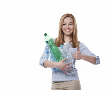 A young woman with long, straight, reddish-blonde hair smiling and giving a thumbs-up while holding a collection of clear plastic bottles with green and blue caps against her chest. She wears a light blue, long-sleeved shirt and beige trousers. The background is plain white, emphasizing her cheerful expression and the bottles. The bottles vary in size and shape, appearing to be used for soft drinks or water, and are made of transparent plastic with textured surfaces and colorful caps. The lighting is even, highlighting the glossy finish of the plastic bottles and her friendly demeanor. This image is relevant to waste management services, suggesting recycling or rubbish collection, and is suitable for a site like Commercial Waste Wanstead, located in the Wanstead area, which offers rubbish removal services.